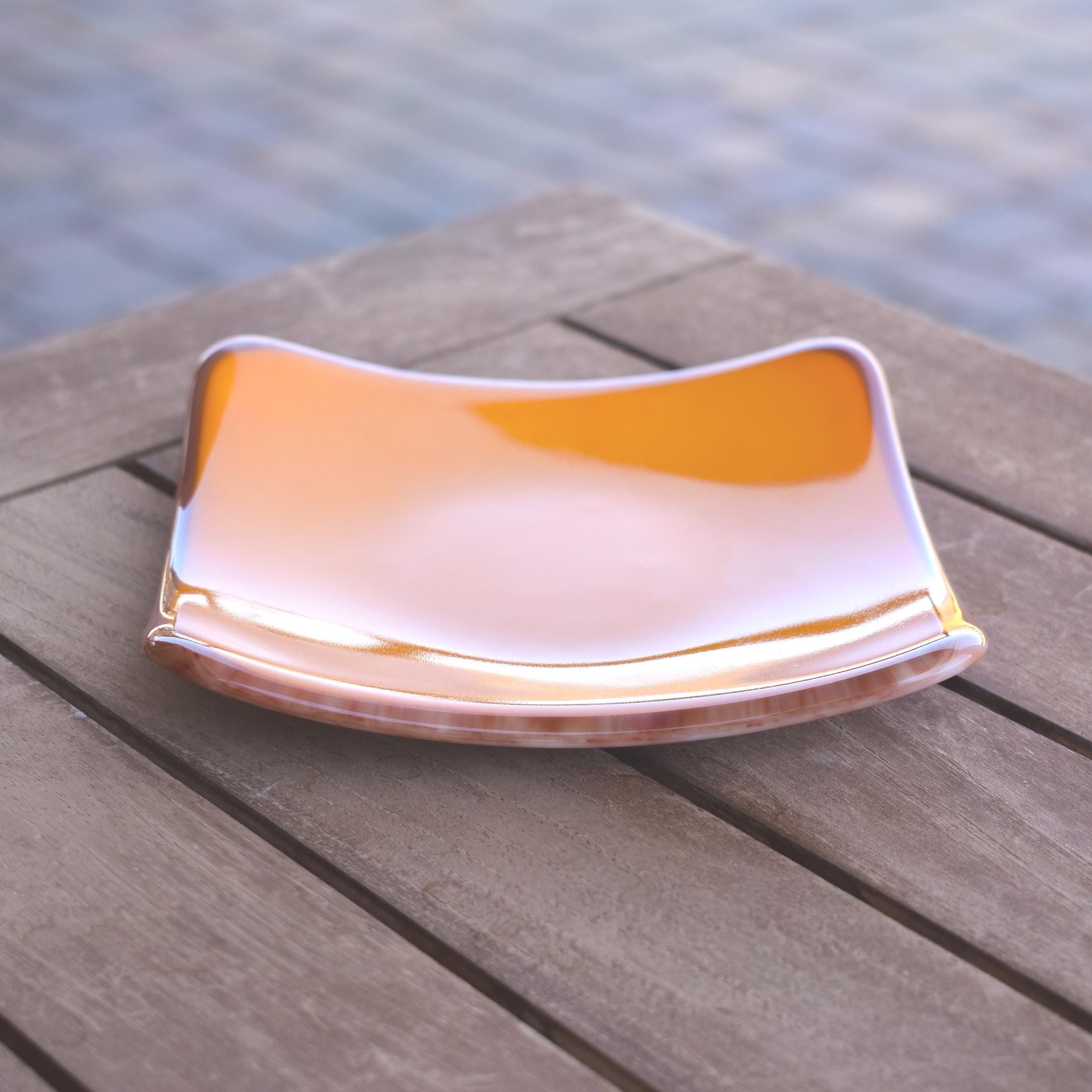 6 inch square fused glass tray with bright opaque orange base and red, orange, and white streaked glass edges and base, resting on slatted wood table.