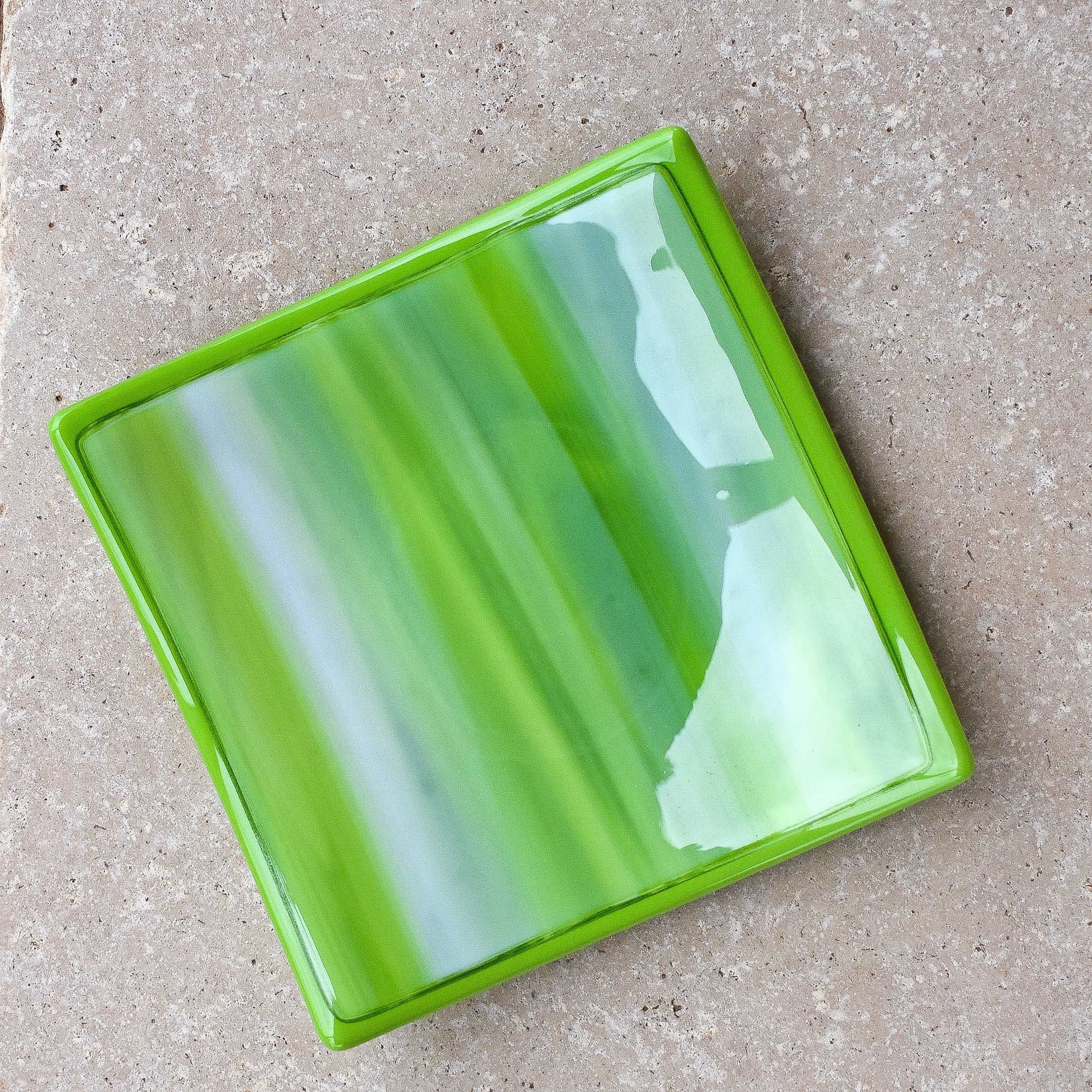 Six inch square fused glass tray in lime green, amazon green and white with amazon green trim, viewed from the top. Tray is sitting on neutral tile.