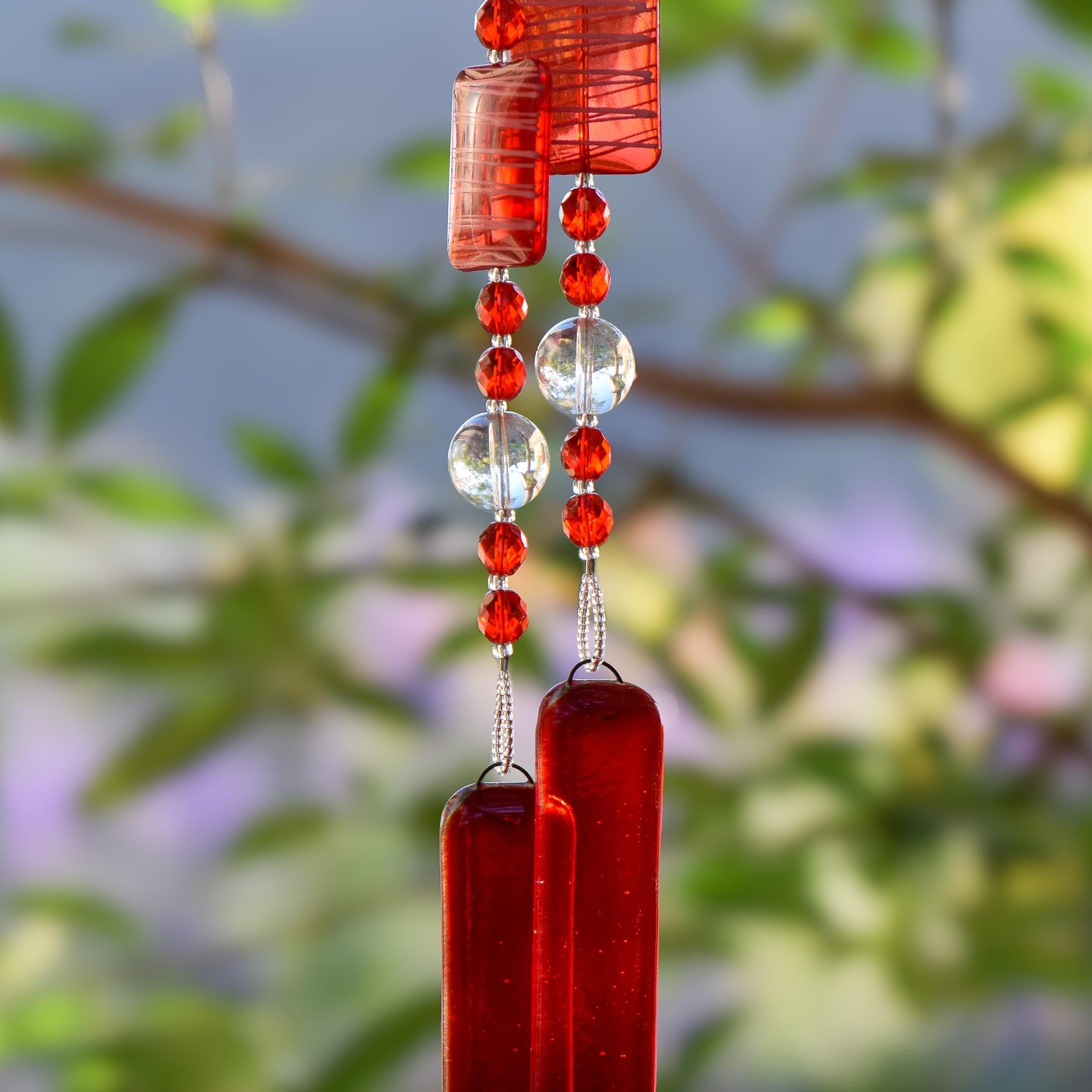 Red wind chime hanging from tree. Chime is made of fused glass, glass beads, stainless steel wire and acrylic rectangular beads.