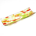 A rectangular glass serving dish with a curved design. The dish features a clear base with green and orange abstract patterns. The colors are swirled and speckled throughout the glass, creating a unique and artistic look. The edges are slightly raised.