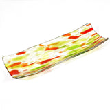 A rectangular glass serving dish with a curved design. The dish features a clear base with green and orange abstract patterns. The colors are swirled and speckled throughout the glass, creating a unique and artistic look. The edges are slightly raised.