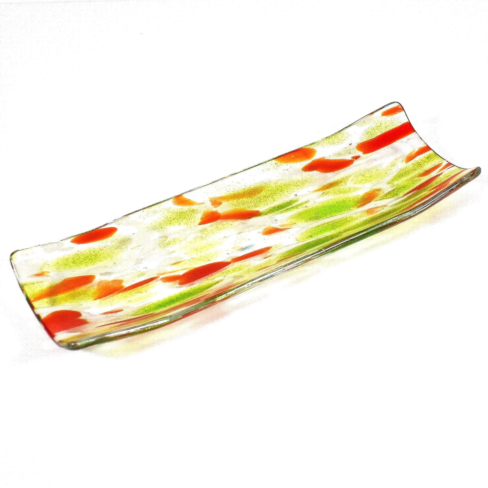 A rectangular glass serving dish with a curved design. The dish features a clear base with green and orange abstract patterns. The colors are swirled and speckled throughout the glass, creating a unique and artistic look. The edges are slightly raised.