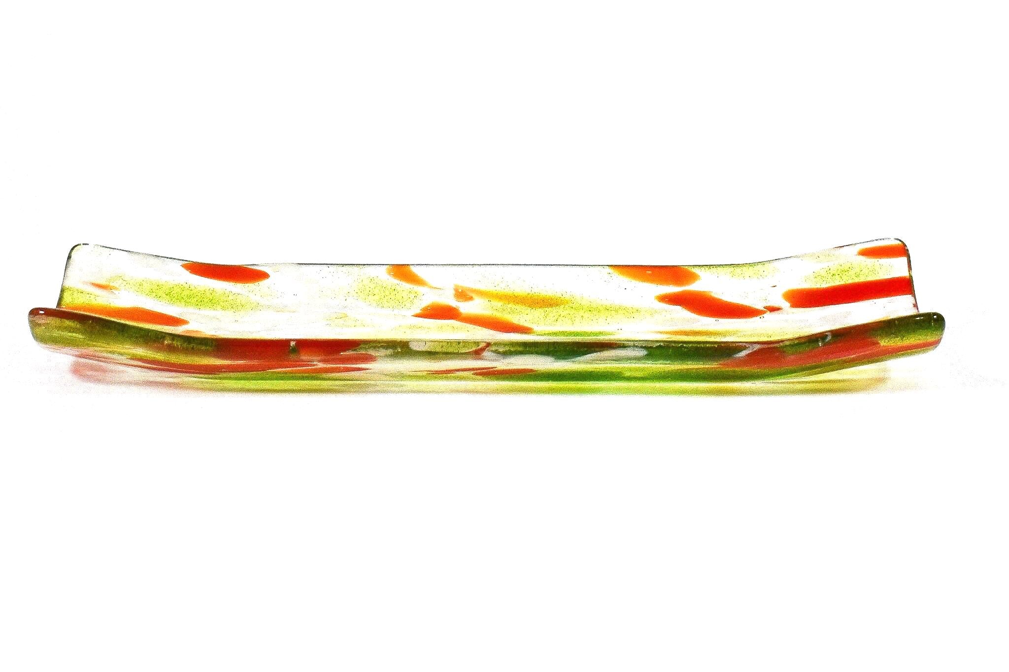 A rectangular glass dish with a curved design. The dish features a clear base with green and orange accents. The colors are distributed throughout the dish, creating a decorative pattern. The dish is likely used for serving or displaying items.