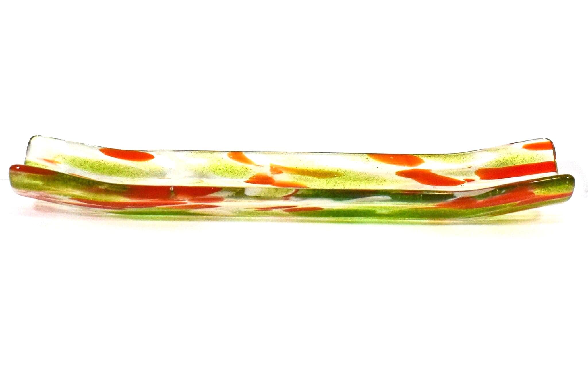 A long, rectangular glass dish with a curved shape. The dish is clear with green and orange color accents. The green is in the form of streaks and the orange is in the form of small, irregular shapes. The dish is likely used for serving or display purposes.