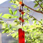 Bottom portion of Cinjo Handmade wind chime hanging from a tree against a background of foliage. The chime is anchored by two rectangular pieces of red and orange fused glass. Above the glass anchors are two strings of beads. The beads are large round carnelian stones and small round red agate stones.