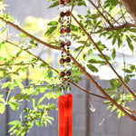 Bottom portion of Cinjo Handmade wind chime hanging from a tree against a background of foliage. The chime is anchored by two rectangular pieces of red and orange fused glass. Above the glass anchors are two strings of beads. The beads are large round carnelian stones, small found carnelian stones and large clear glass beads.