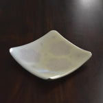 Six inch square glass tray in vanilla cream with a flowery design sitting on a dark wood table.
