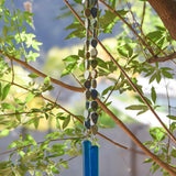 Cinjo Handmade wind chime hanging from tree with foliage in blurred background. Two legs of genuine azurite-malachite stones, roughly cut and with a matte finish are strong on wire and hanging with transparent blue glass pieces at the bottom of each.