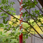 Handmade red, orange and white fused glass wind chime hanging outdoors among green leaves.
