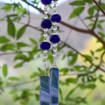 Handmade cobalt blue fused glass wind chime with authentic African Krobo beads and clear glass accent beads hanging outdoors among green leaves.