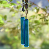 Cinjo Handmade wind chime hanging from tree with foliage in blurred background. Two legs of genuine azurite-malachite stones, roughly cut and with a matte finish are strong on wire and hanging with transparent blue glass pieces at the bottom of each.