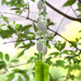 Handmade lime green fused glass wind chime with white chrysoprase stones and faceted green glass beads hanging from a flowering tree branch outdoors.