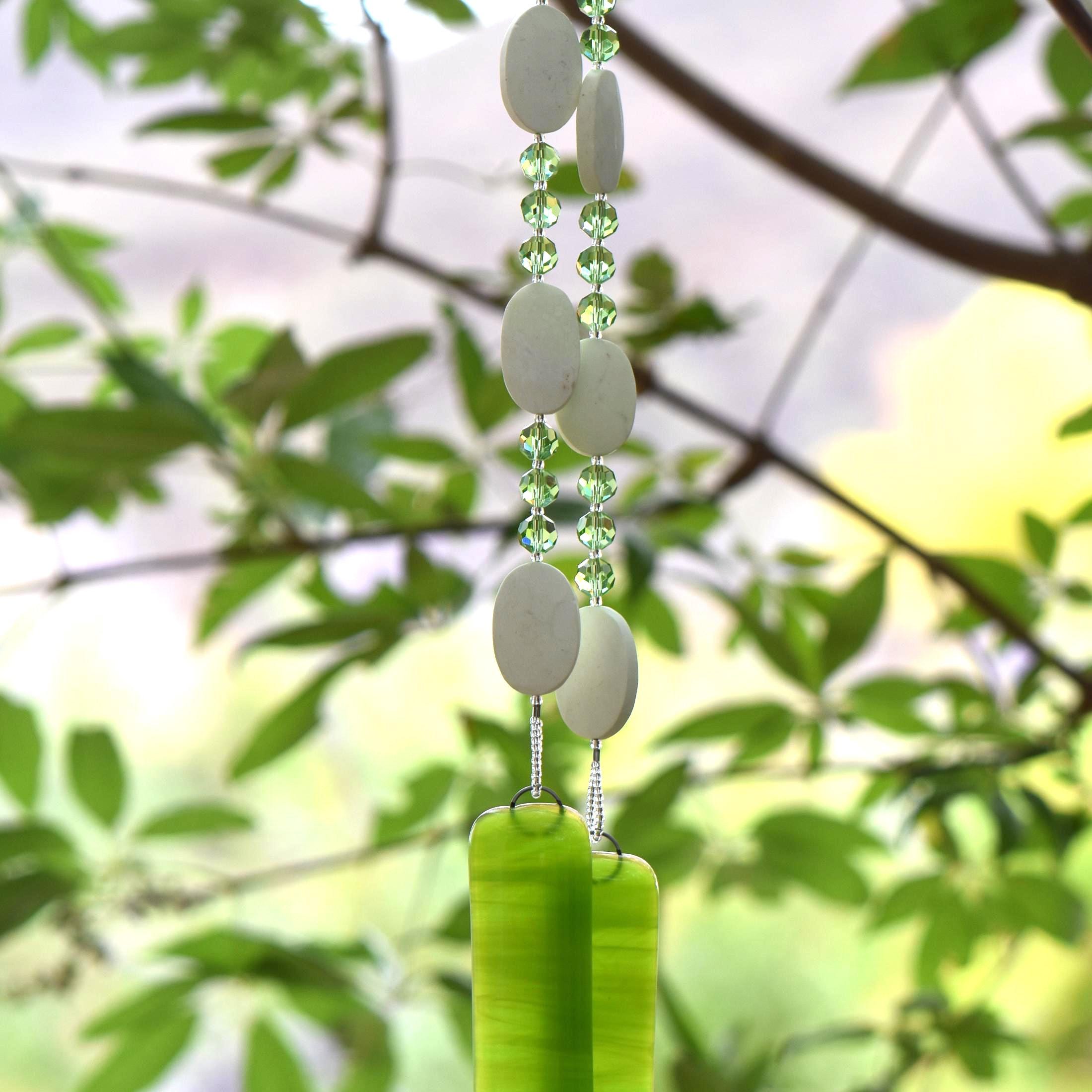 Handmade lime green fused glass wind chime with white chrysoprase stones and faceted green glass beads hanging from a flowering tree branch outdoors.