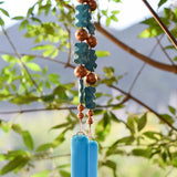 Handmade turquoise blue glass wind chime with blue magnesite stones and copper beads hanging from a tree in warm afternoon sunlight.