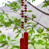 Cinjo Handmade wind chime hanging from a tree with green foliage background. Two strands of stainless steel with faceted carnelian stone rondelle shaped beads accented with large clear glass beads, anchored by two pieces of red fused glass with orange swirls.