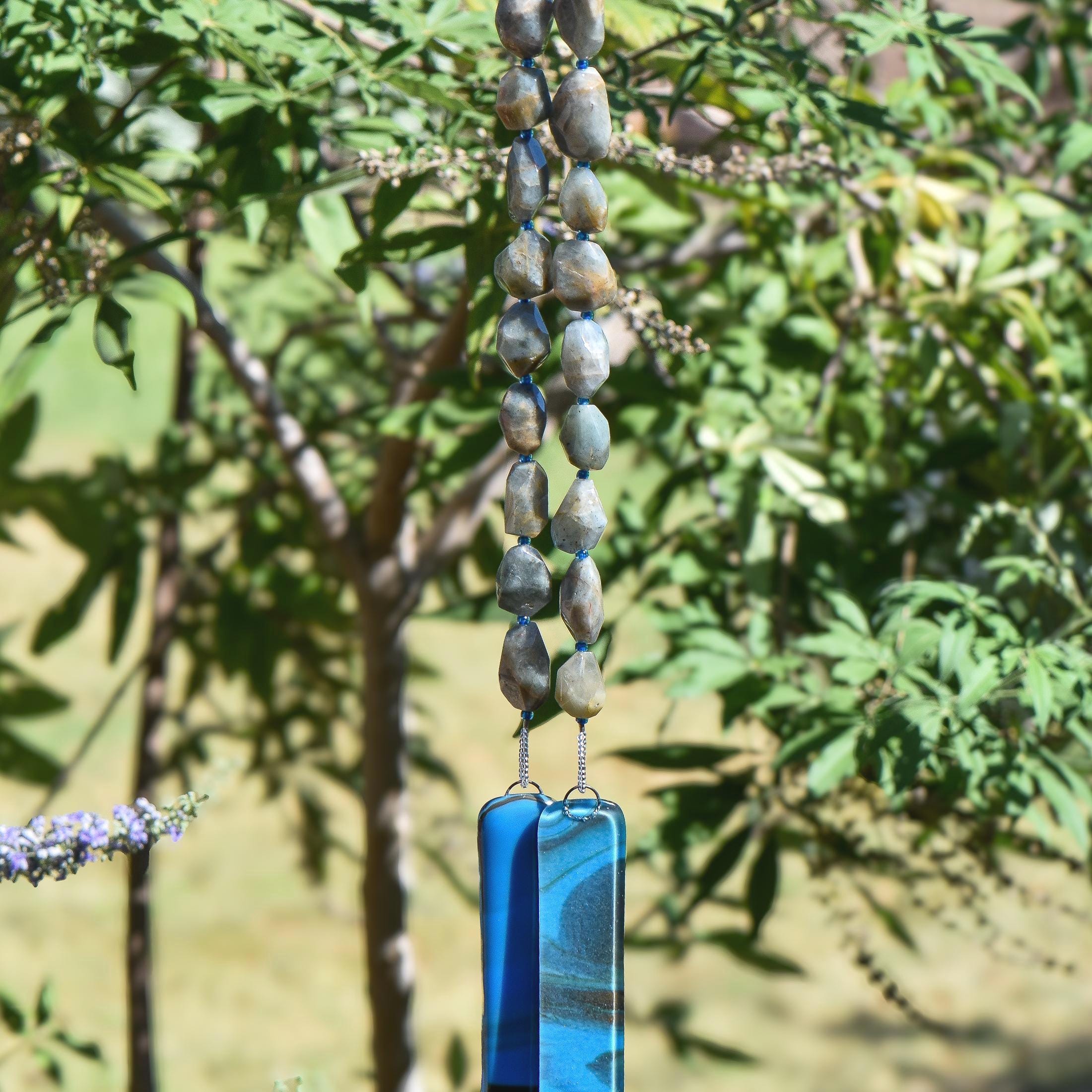 Lodolite stone wind chime with earthy translucent gemstone beads and handmade blue fused glass pieces, hanging outdoors against a softly blurred background.
