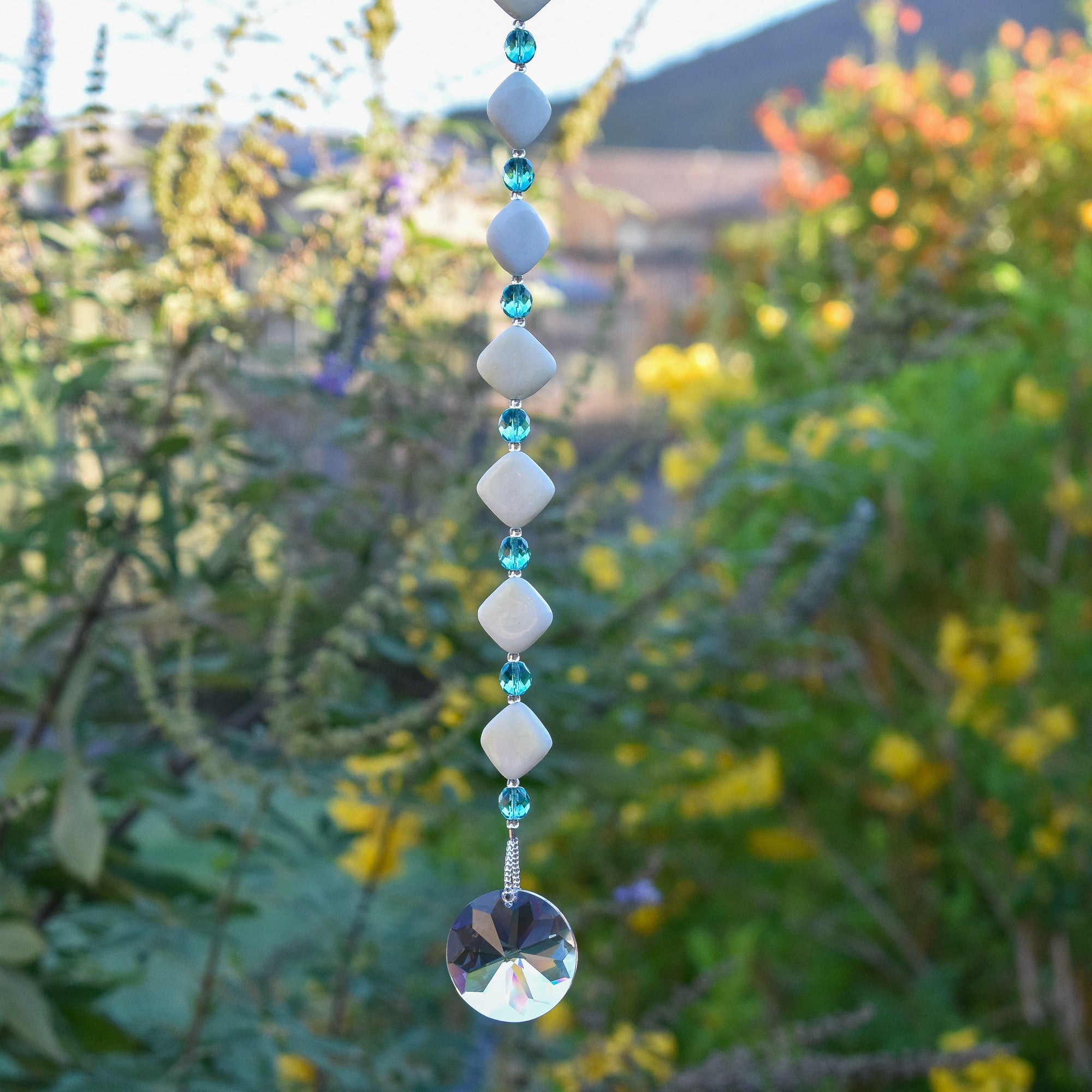 Decorative hanging with diamond-shaped stone beads and a crystal in front of a blurred garden background