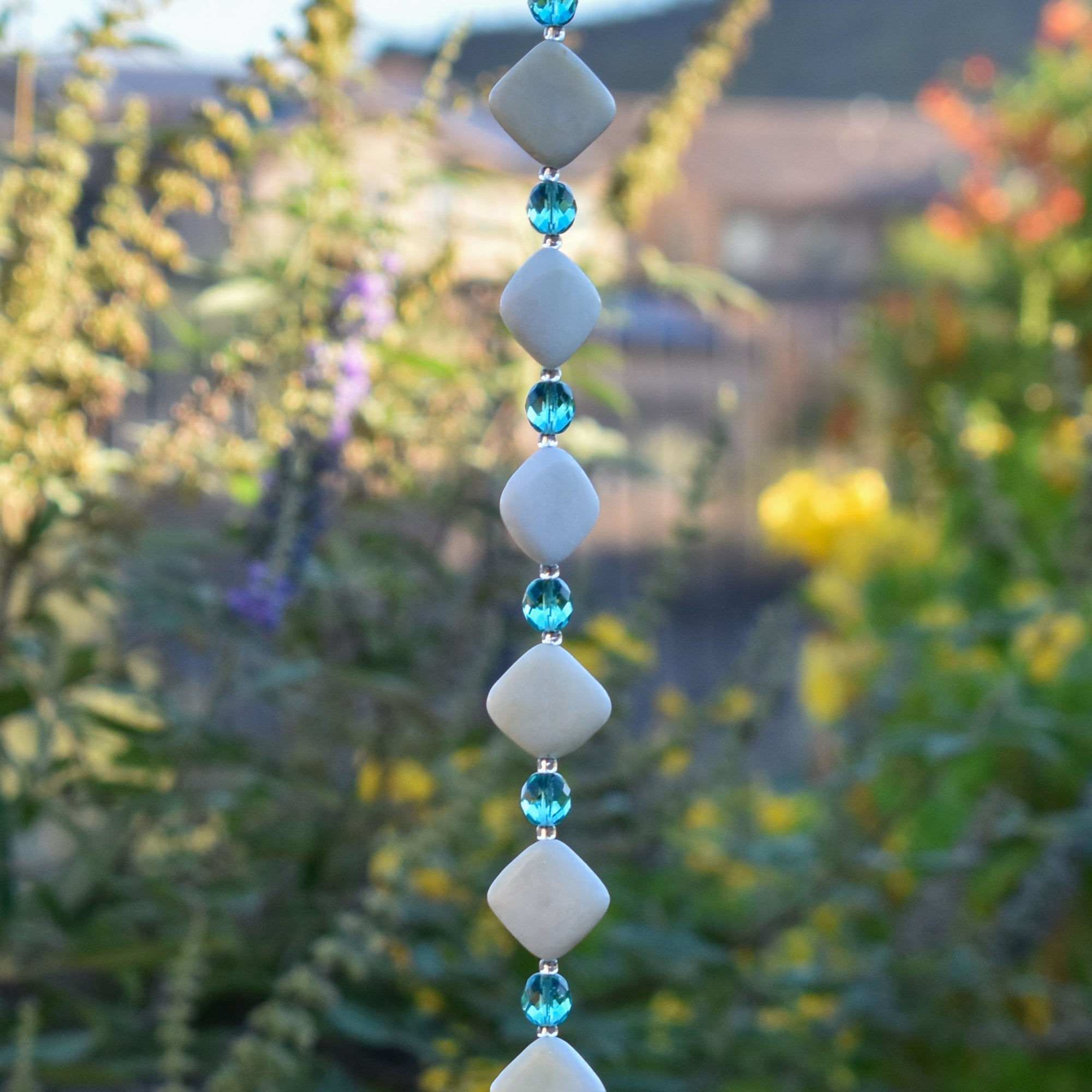 Decorative hanging with diamond-shaped stone beads and light aqua faceted glass beads against blurred landscape background.