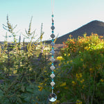 Decorative hanging with diamond-shaped stone beads and light aqua faceted glass beads against blurred landscape background.