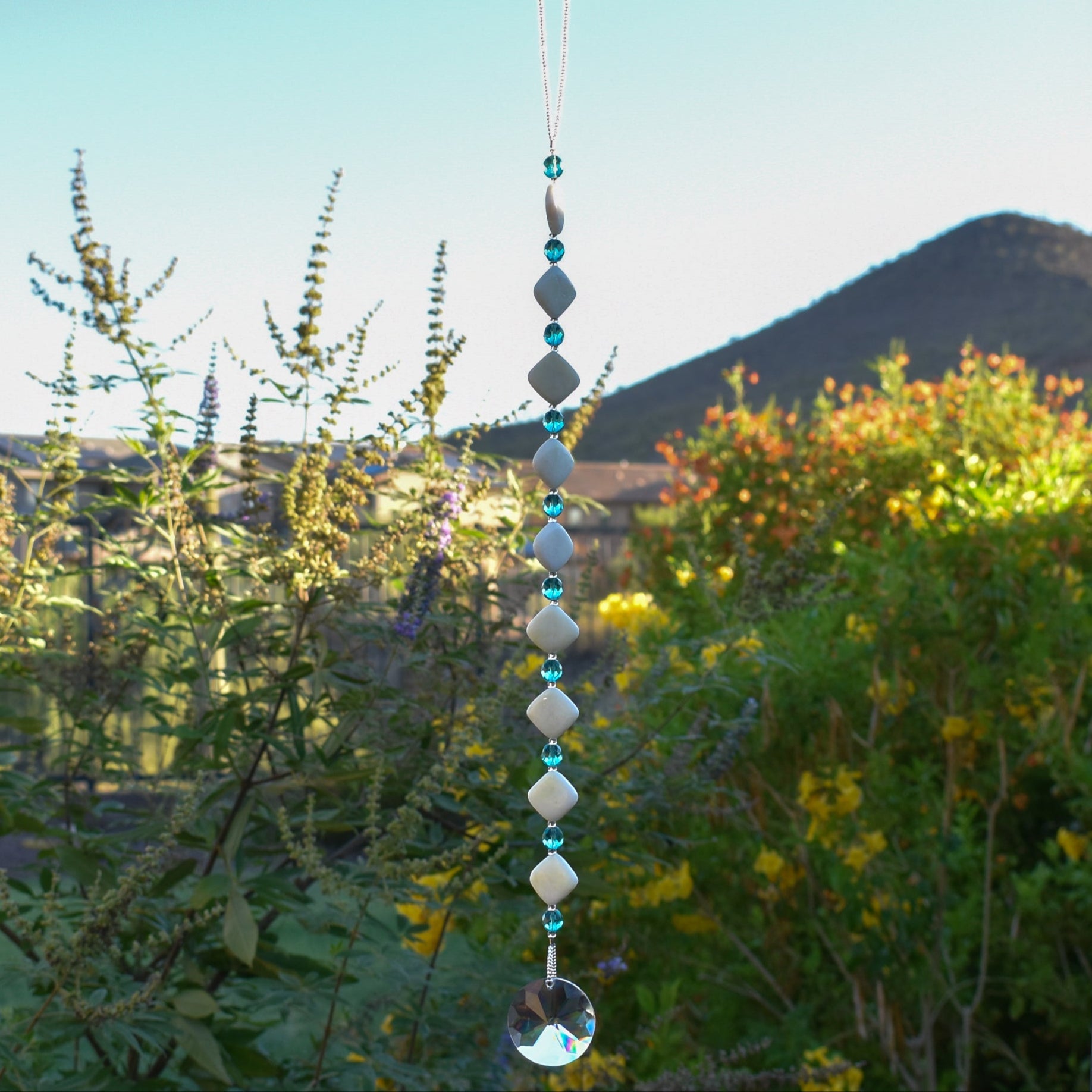 Decorative hanging with diamond-shaped stone beads and light aqua faceted glass beads against blurred landscape background.