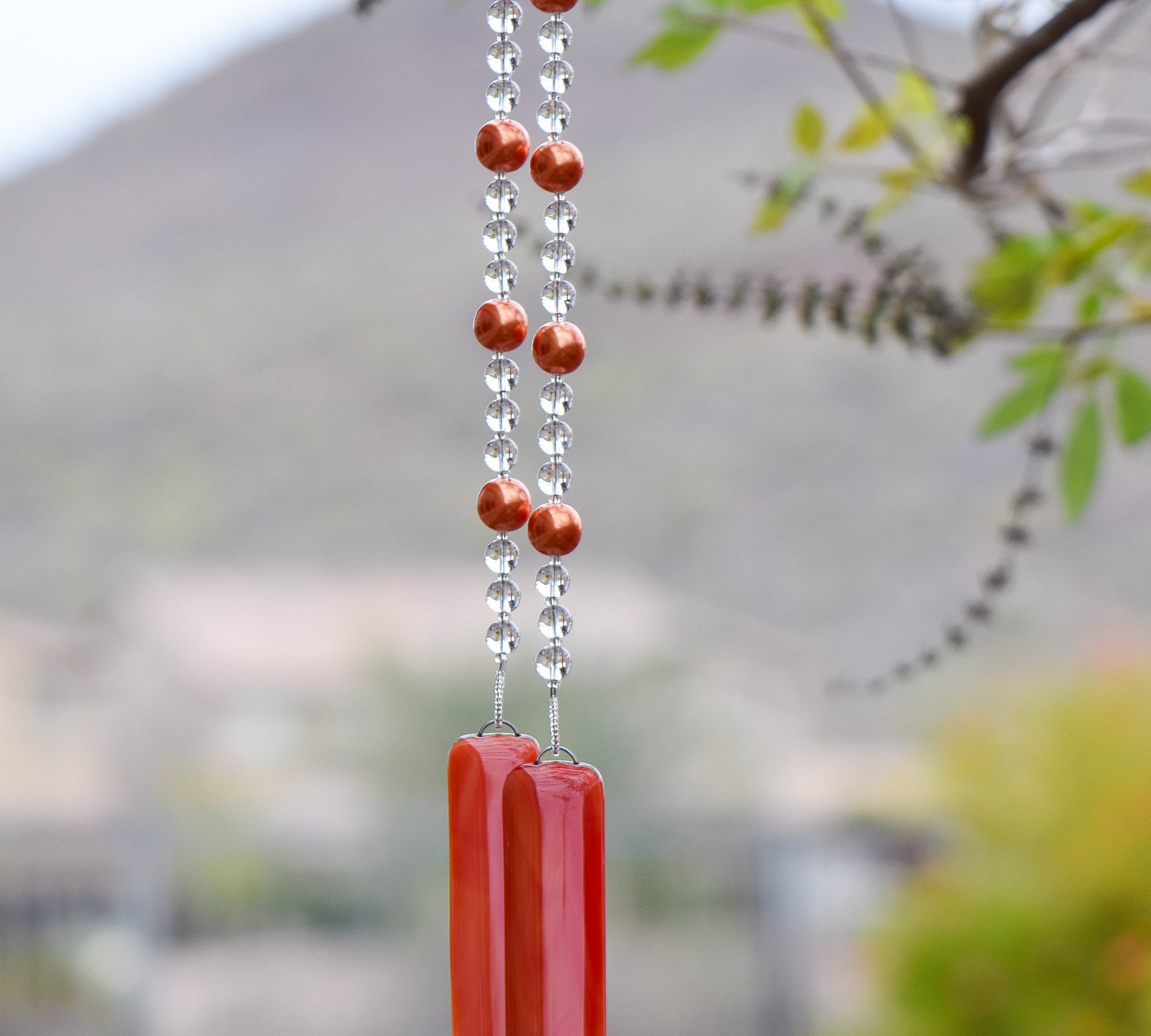 bright neon orange glass beads paired with clear glass beads, strung on wire and hanging vertically. anchored by two orange pieces of fused glass