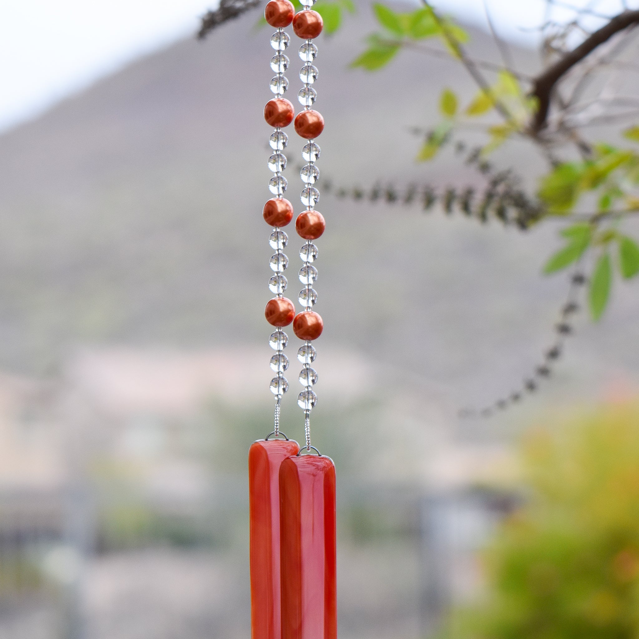 bright neon orange glass beads paired with clear glass beads, strung on wire and hanging vertically. anchored by two orange pieces of fused glass
