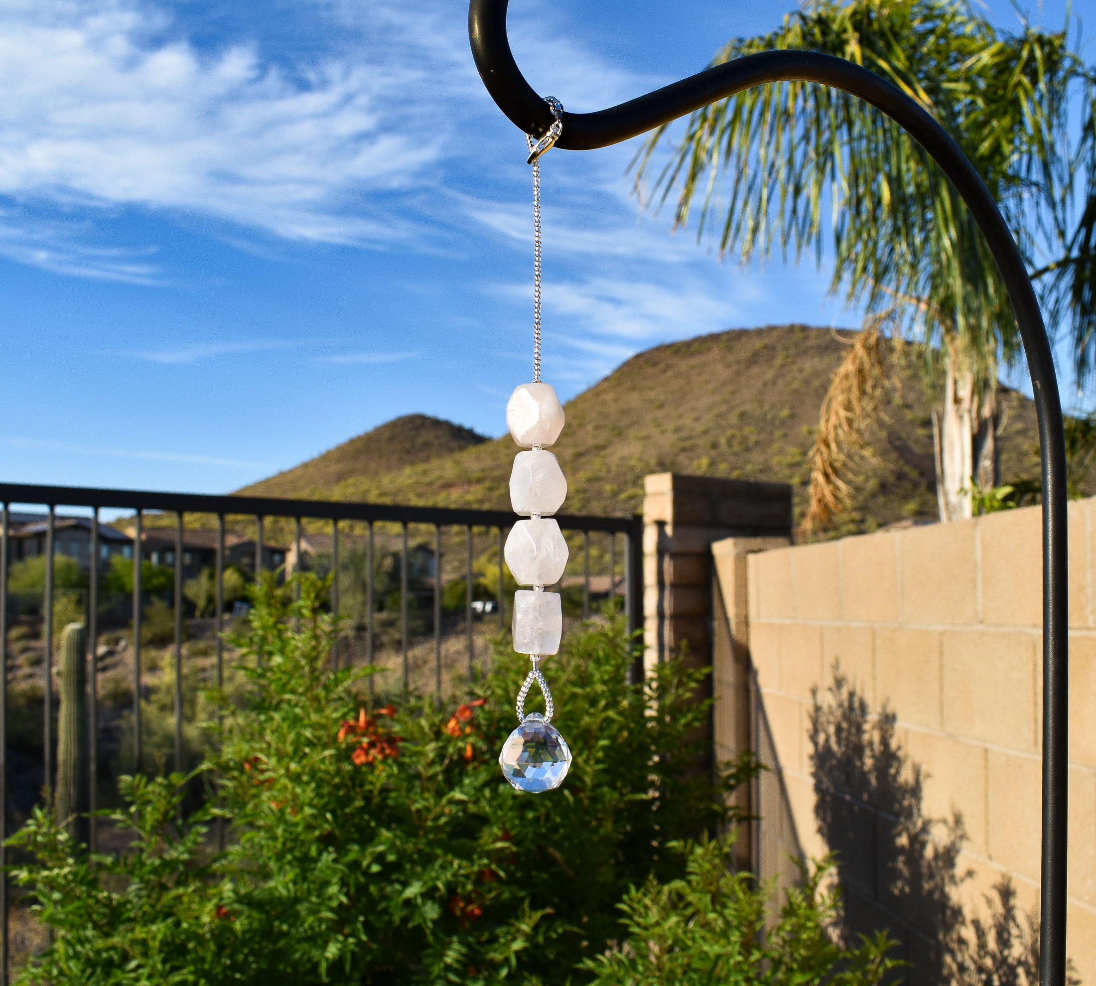 Four rose quartz stones strung vertically with a small round crystal prism at the bottom, in a suburban setting.