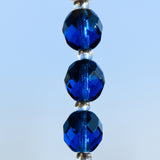 3 Small deep aqua blue glass beads hung vertically against sky background.
