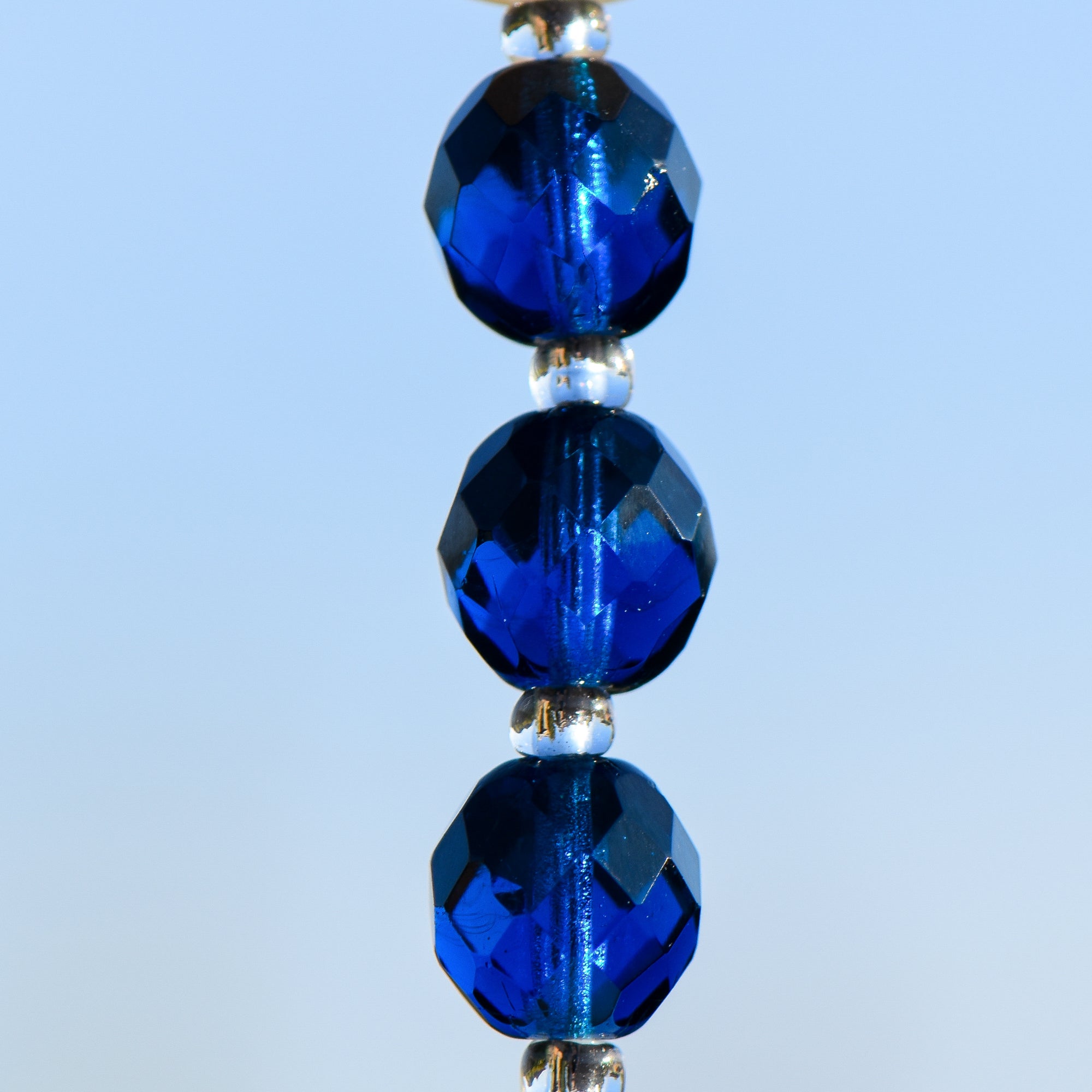 3 Small deep aqua blue glass beads hung vertically against sky background.