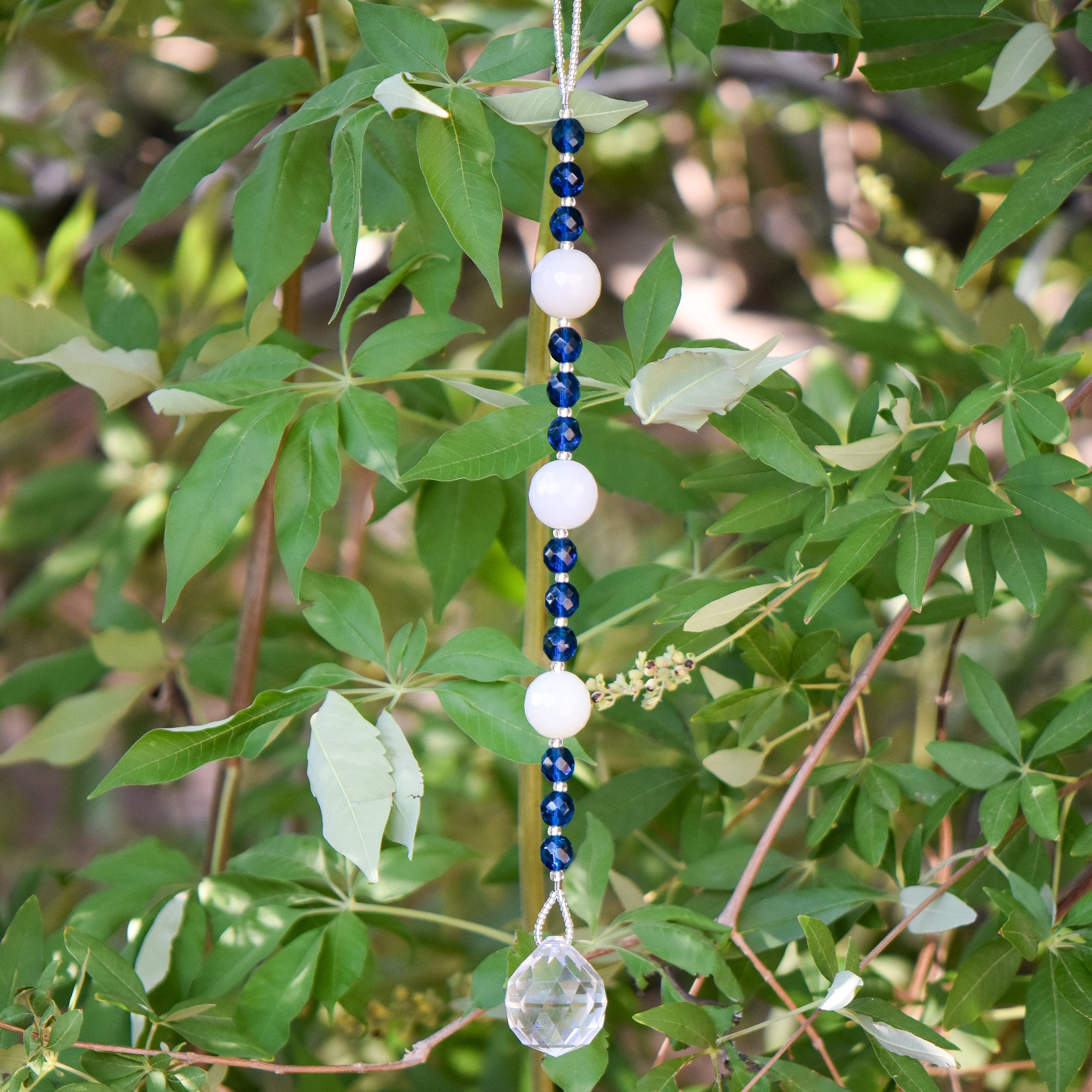 Quartz and Aqua Glass Sun catcher hanging vertically against background of leaves.