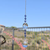 Large, clear glass crystal oval bead hanging vertically with 3 purple crystal beads above and 3 below, anchored by small round crystal prism.