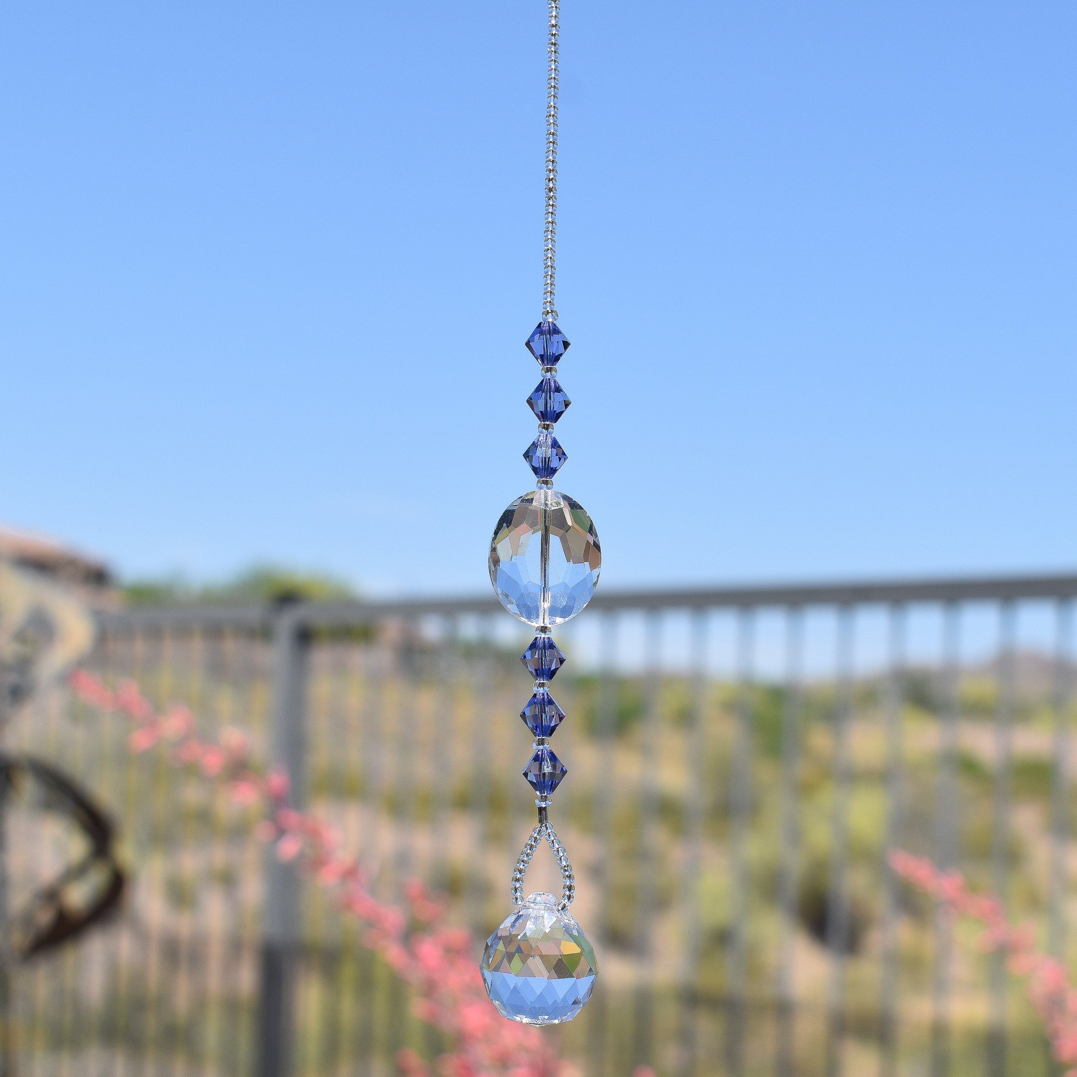 Large, clear glass crystal oval bead hanging vertically with 3 purple crystal beads above and 3 below, anchored by small round crystal prism.
