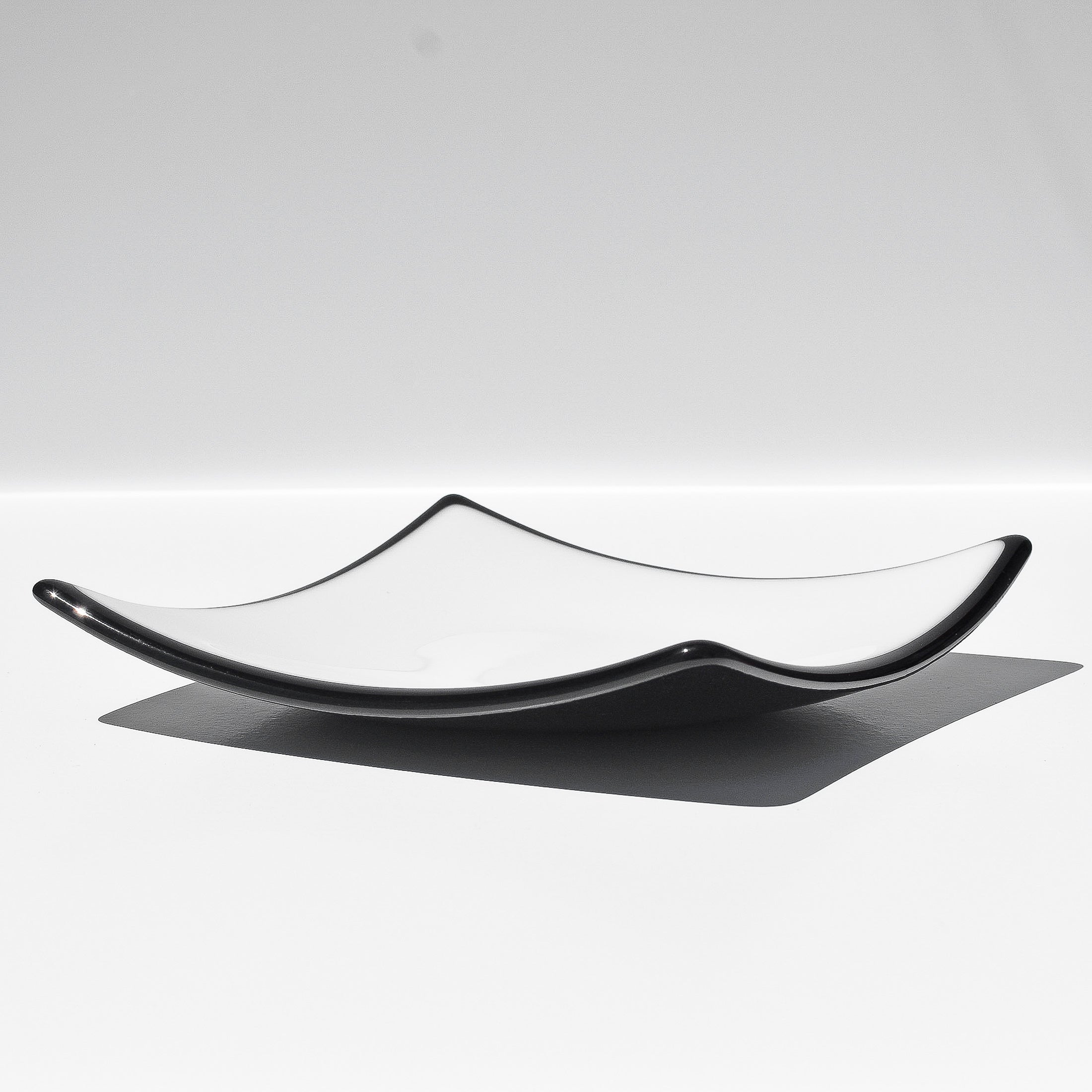 White square dish with black trim on white background viewed from the side
