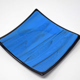 Square blue glass dish with black trim and black designs in the glass, on white background.