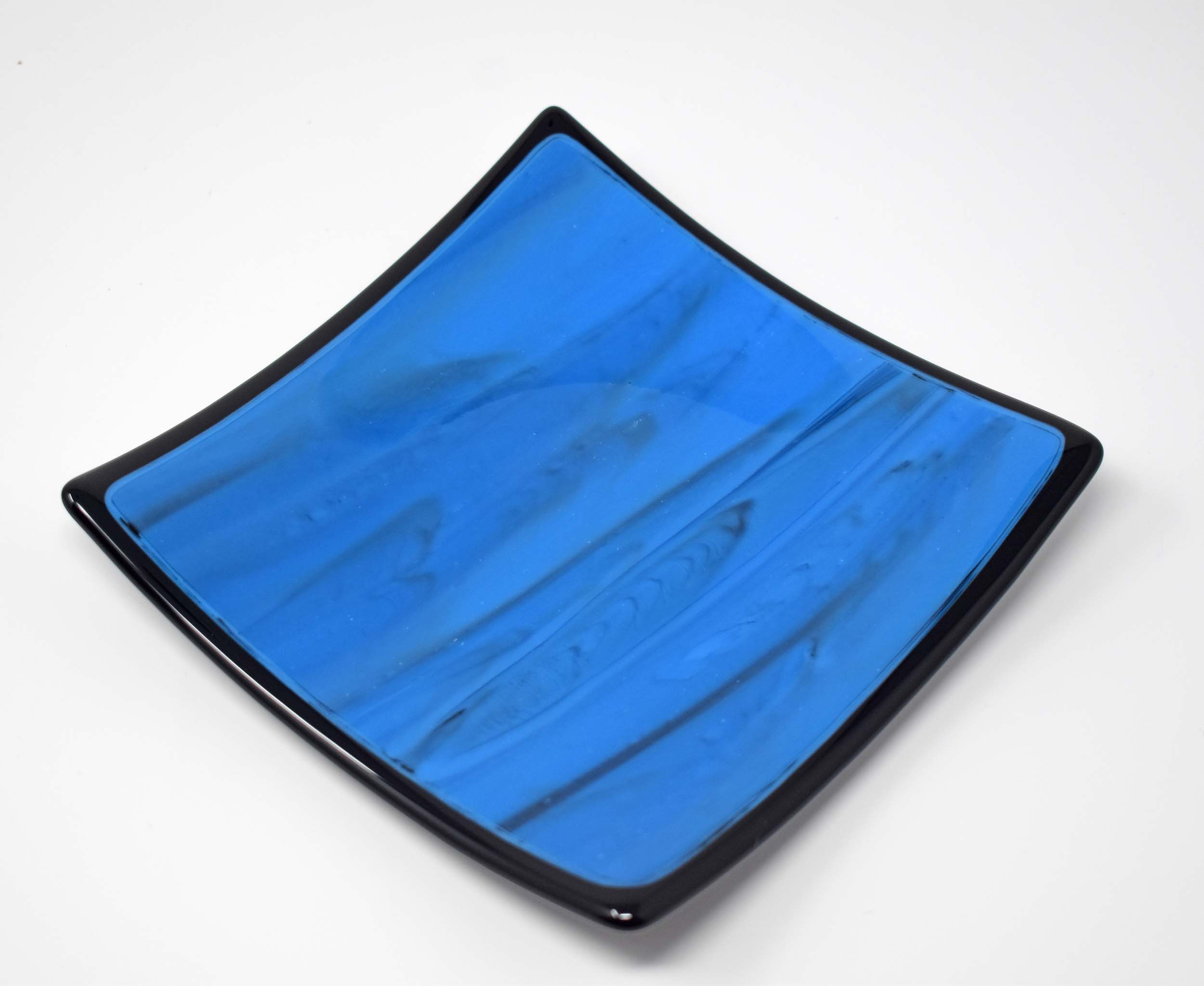 Square blue glass dish with black trim and black designs in the glass, on white background.