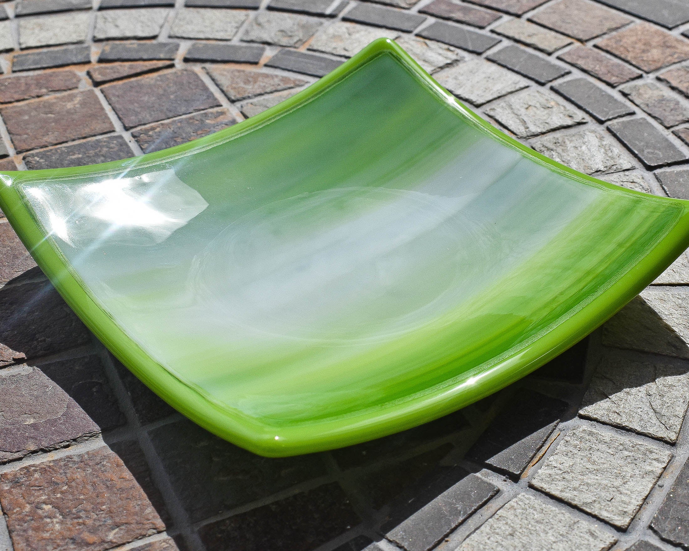 Small, square glass dish in lime green and white on stone table