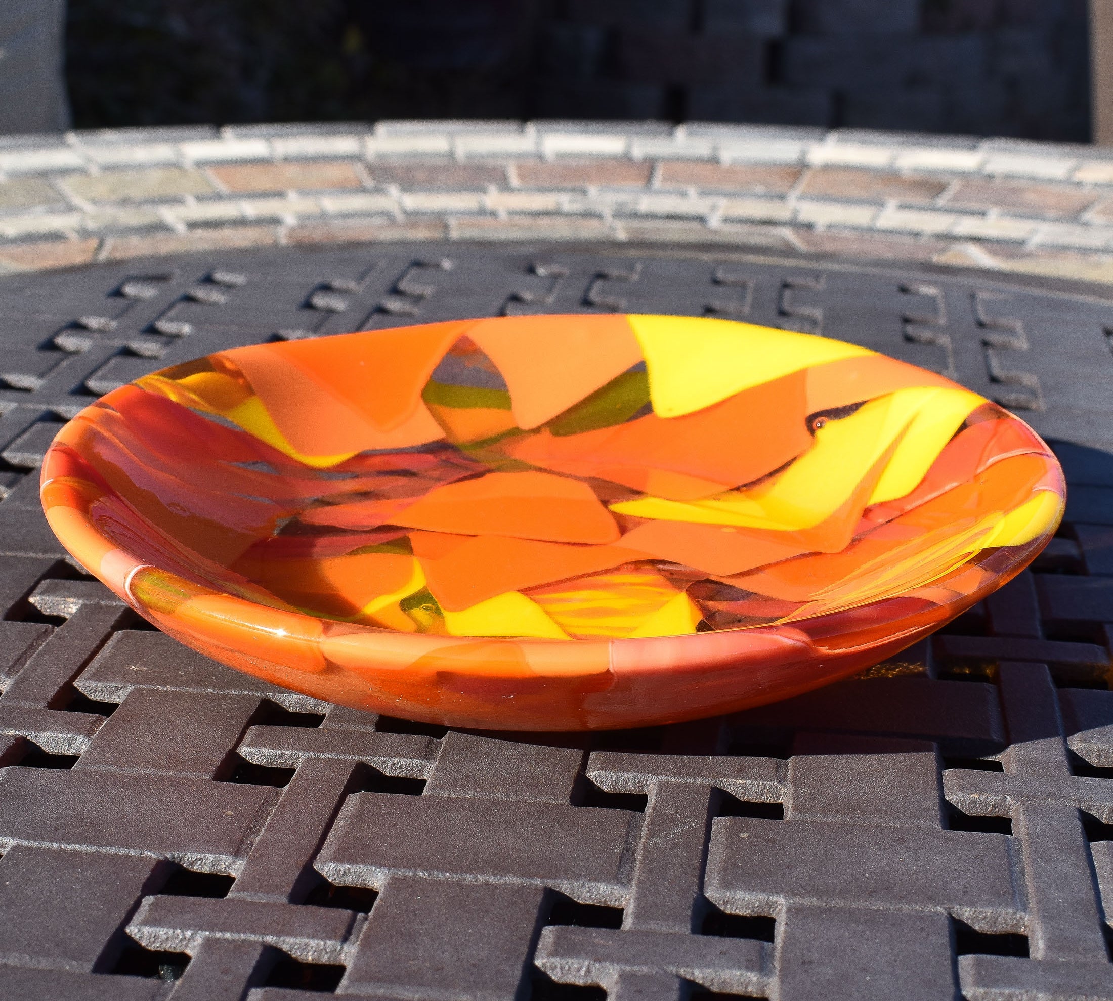 orange and yellow round fused glass bowl on metal grid