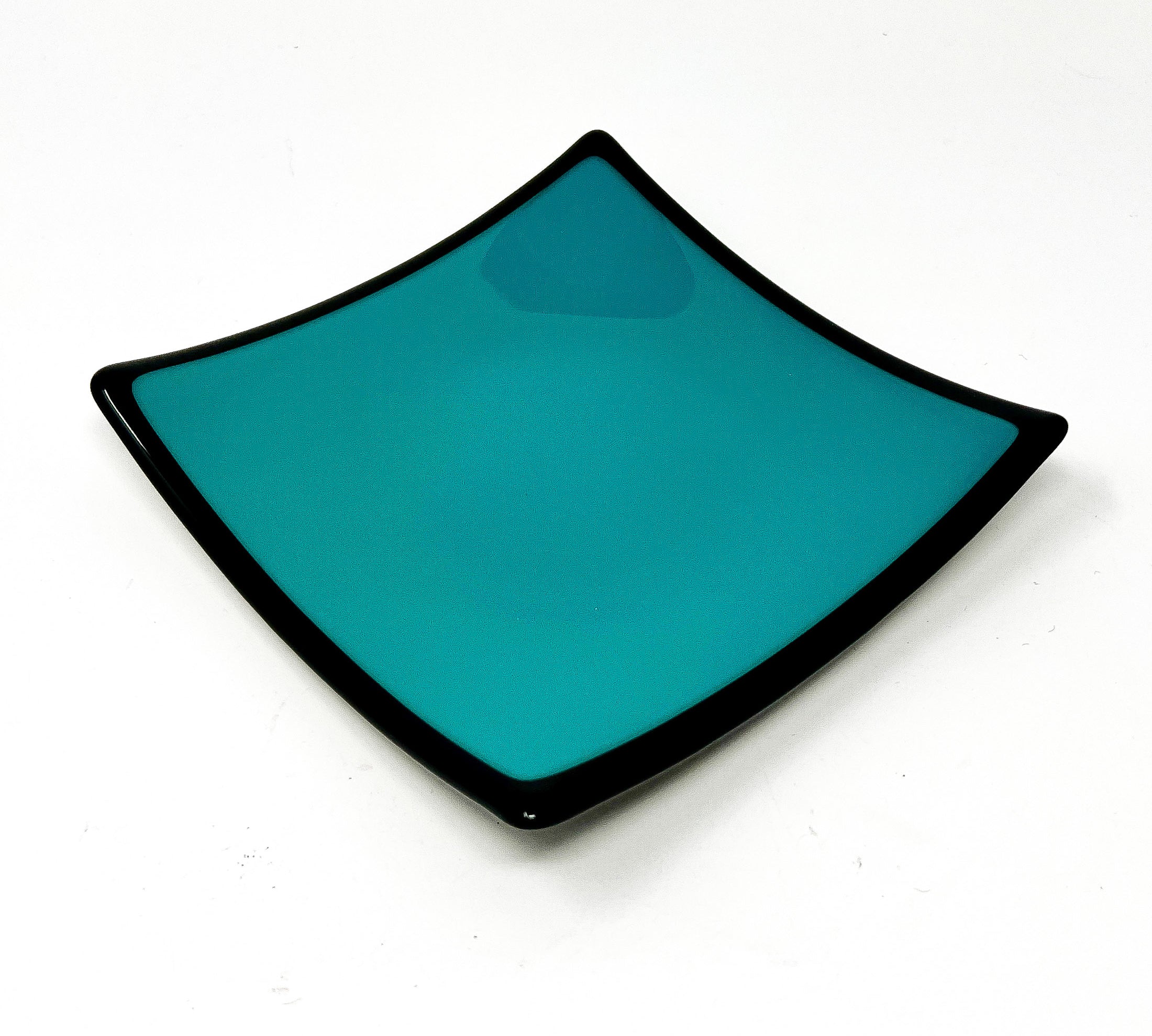 Square glass dish in teal green with black rim in front of white background