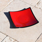 Red glass dish with black trim on travertine pavers