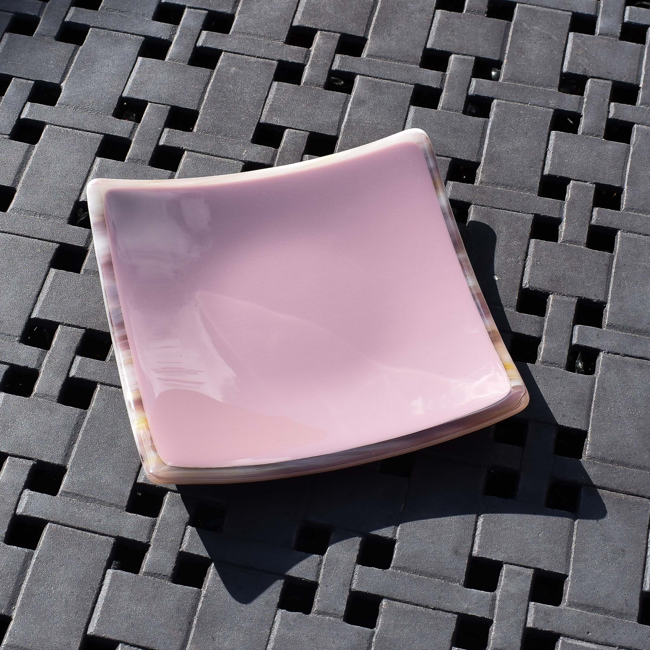 Violet/light purple fused glass dish that is 6" square with multi-color rim and back on a steel grid.