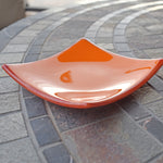Orange and red square dish on mosaic stone table. Dish is orange on top, orange/white/red on bottom and on trim. Slightly sloped.