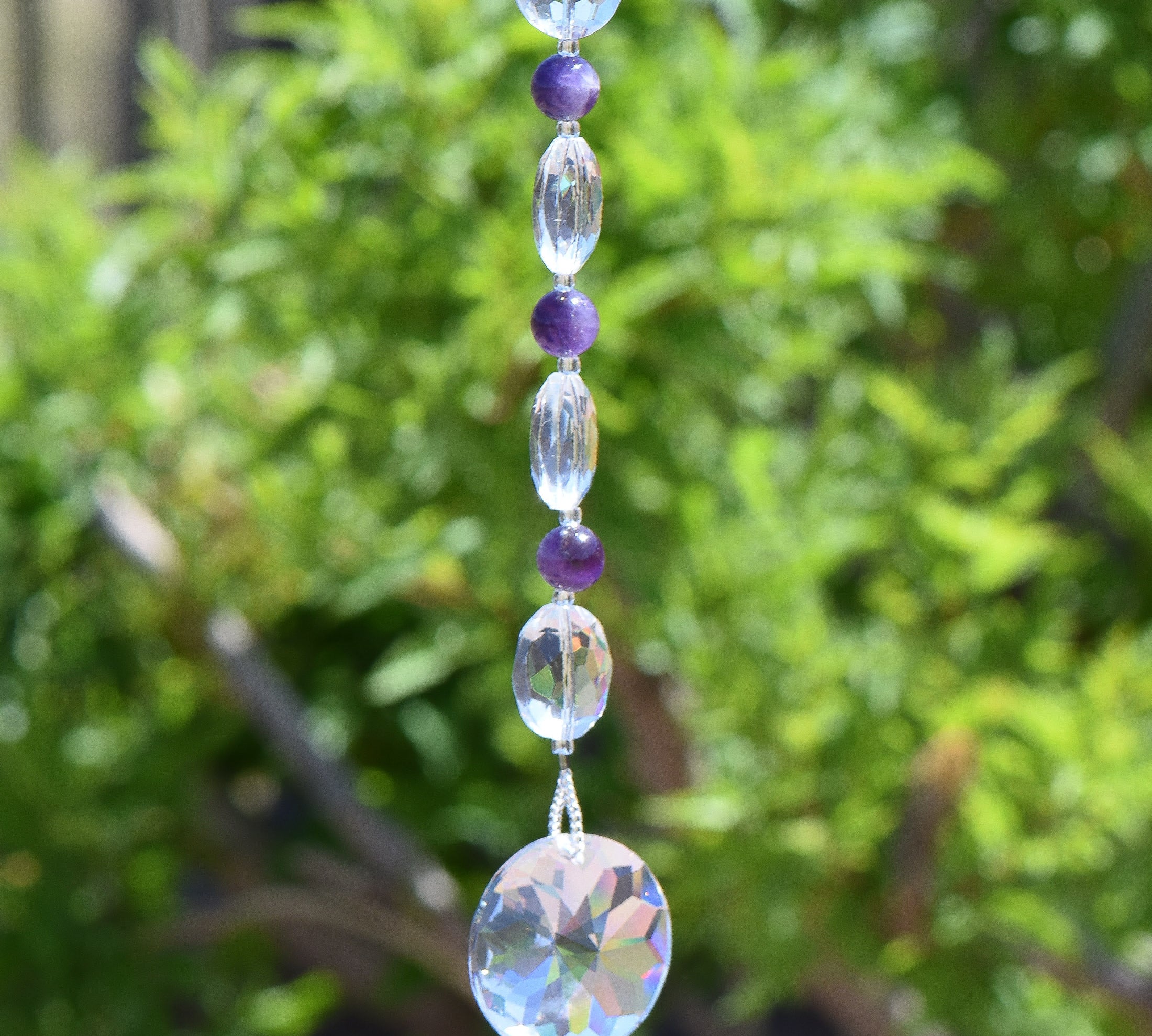 Round amethyst beads strung with faceted glass beads, hanging vertically, anchored by round disc crystal prism.