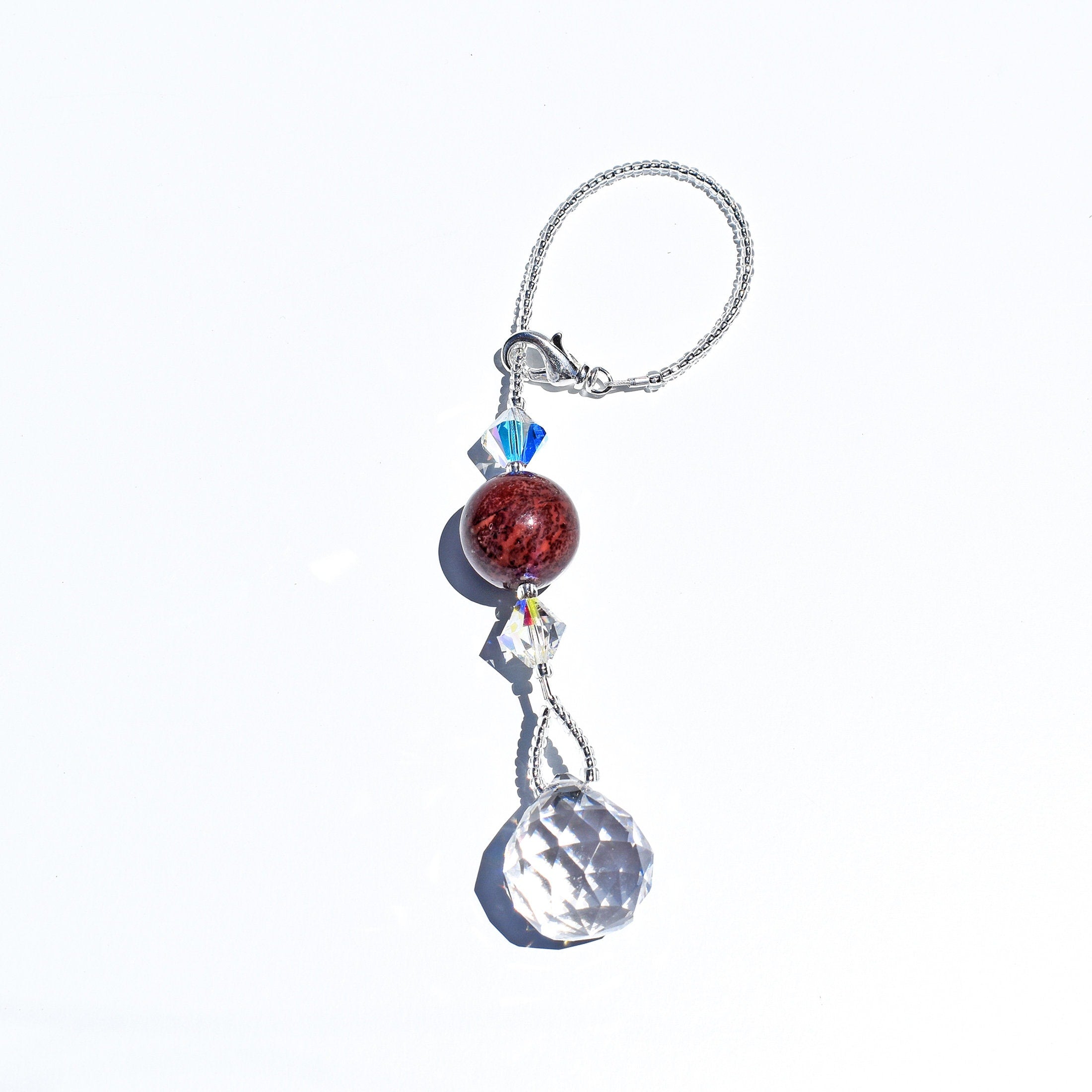 Small sun-catcher strung on wire, laying flat on white background. Includes large zebra jasper stone, flanked by crystal bicone beads, anchored by round crystal prism.