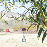 Round jasper stone strung with two bicone crystal beads and anchored by round crystal prism, hanging from tree