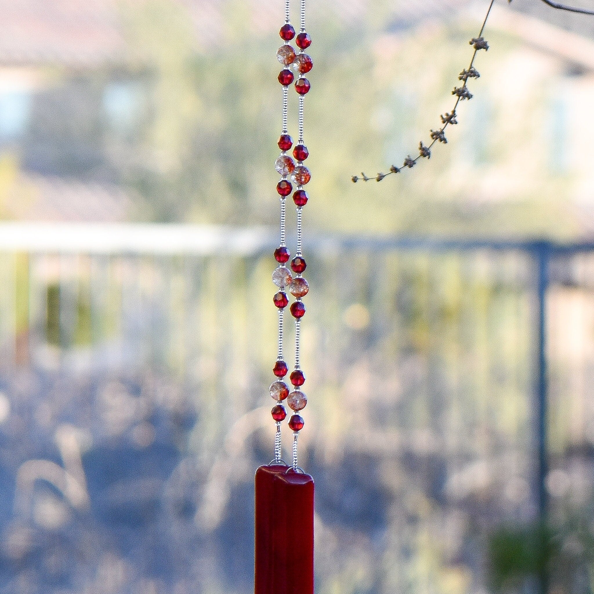Handmade wind chime made with Red Ruby Moss Crystal stones flanked by Austrian crystal beads, anchored by two pieces of red fused glass, hanging from tree