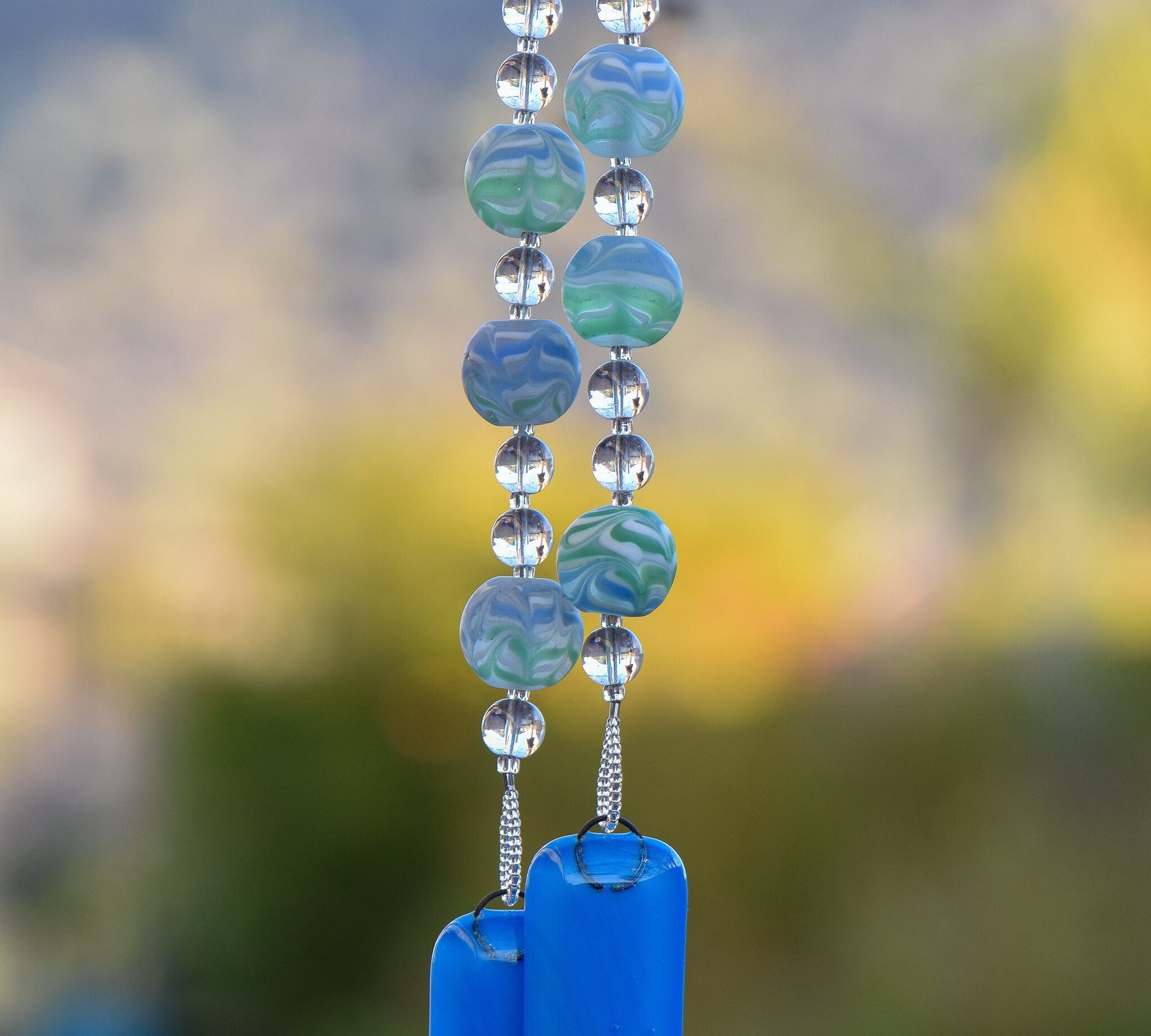 Large green and blue swirl beads strung with smaller clear glass beads and anchored by two blue fused glass pieces, hanging from tree. Handmade. One of a kind.