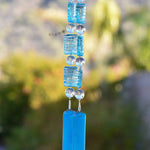 Blue acrylic puffed rectangle beads with white stripes hung with large lamp-worked clear glass beads and anchored by two pieces of sky blue glass, hanging vertically from tree