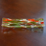clear glass channel-shaped tray with orange, lime green and white design, resting on wood table.