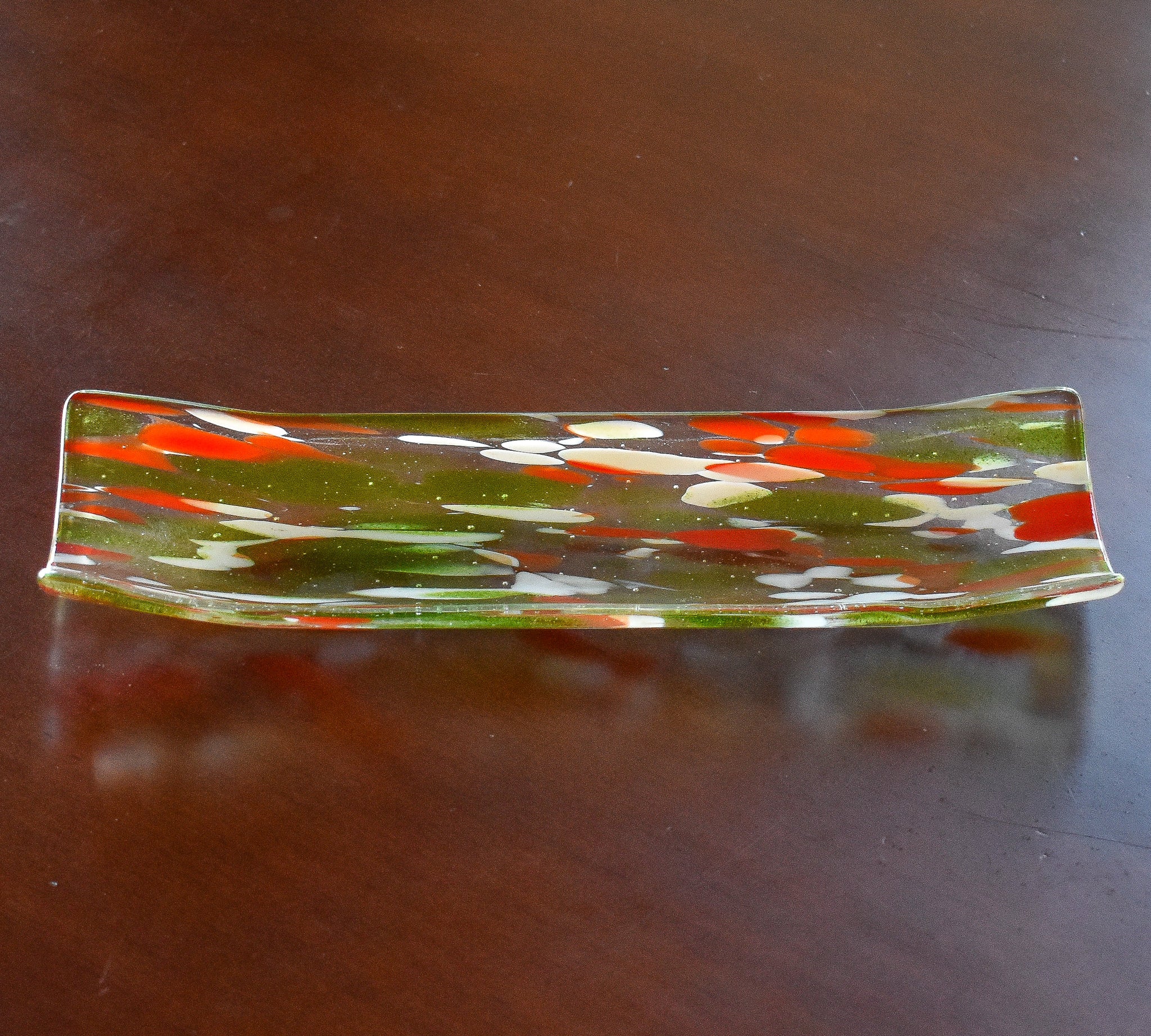 clear glass channel-shaped tray with orange, lime green and white design, resting on wood table.