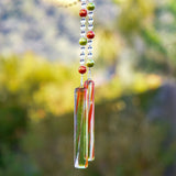 LIme green and bright orange pearl beads strung with smaller clear beads, hanging vertically from a tree, anchored by two pieces of clear/orange/green glass.